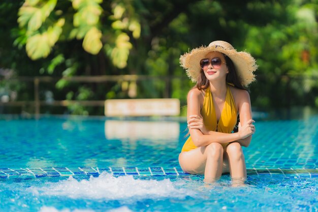 El ocio asiático joven hermoso de la mujer del retrato relaja sonrisa y feliz alrededor de piscina en centro turístico del hotel