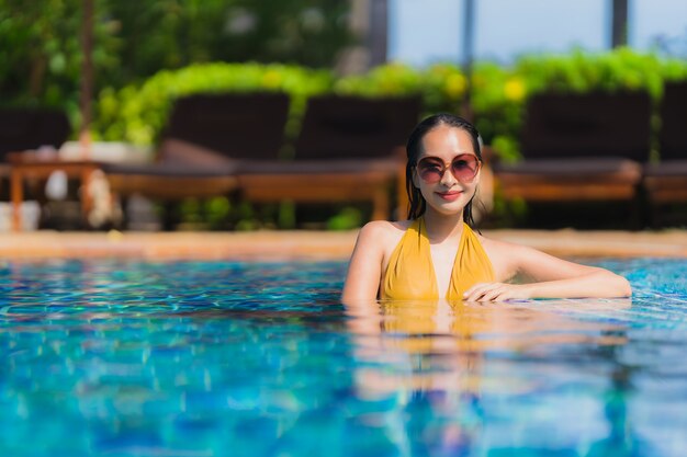 El ocio asiático joven hermoso de la mujer del retrato relaja sonrisa y feliz alrededor de piscina en centro turístico del hotel