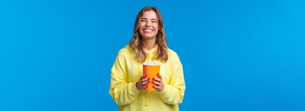 Ocio, diversión y concepto de juventud amable mujer europea rubia feliz disfrutando los fines de semana comiendo palomitas de maíz a