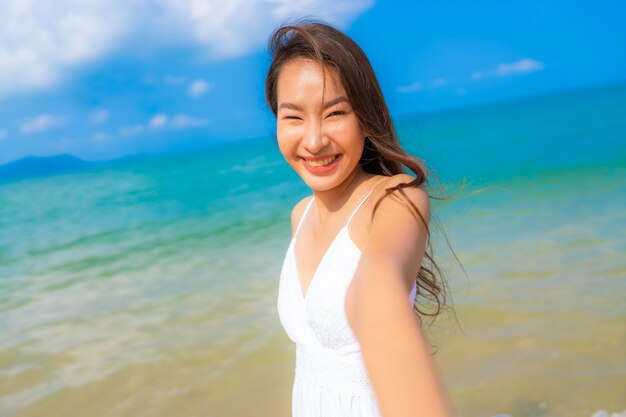 Ocio feliz de la sonrisa de la mujer asiática joven hermosa del retrato en el mar y el océano de la playa