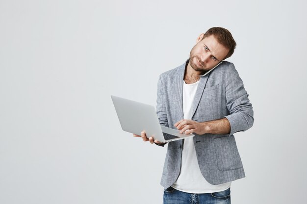 Ocupado apuesto hombre de negocios hablando por teléfono y usando laptop