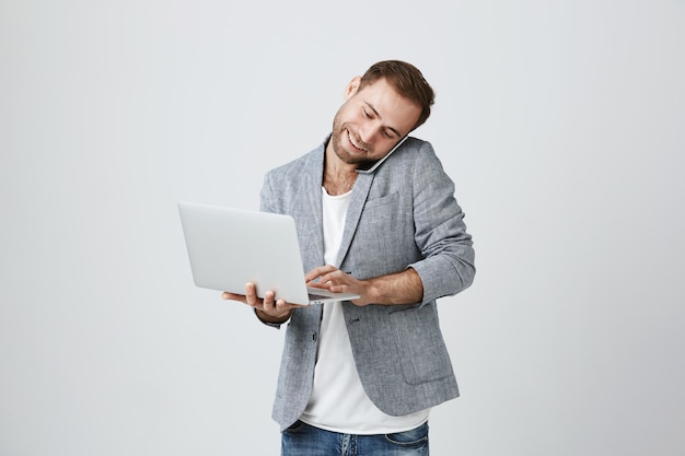 Ocupado apuesto hombre de negocios hablando por teléfono y usando laptop