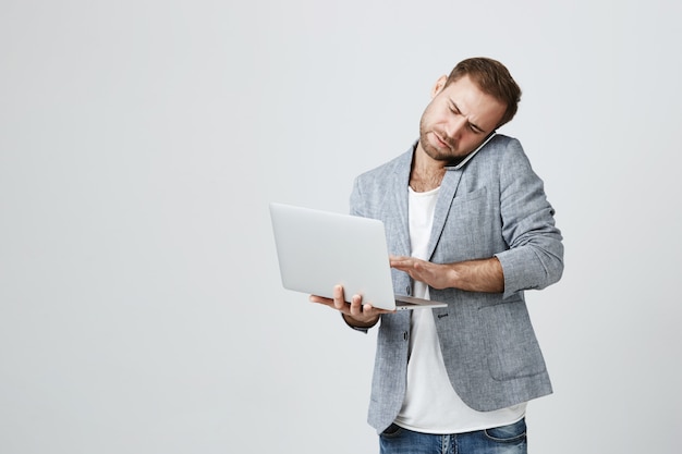 Ocupado apuesto hombre de negocios hablando por teléfono y usando laptop