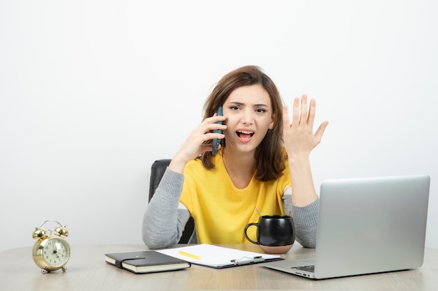 Foto gratuita oficinista sentada en el escritorio y hablando por teléfono móvil.