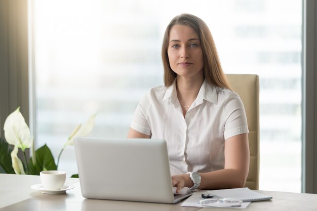 Oficinista de sexo femenino que hace trabajo diario en la computadora portátil