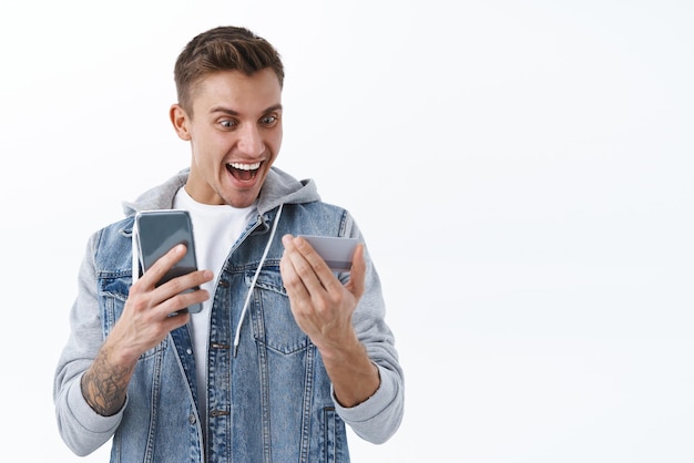 Oh, Dios mío, gané Concepto de celebración y premios Retrato de un joven rubio mirando la tarjeta de crédito divertido y emocionado sonriendo feliz apúrate para pedir una tienda en línea con un gran descuento para mantener el teléfono inteligente