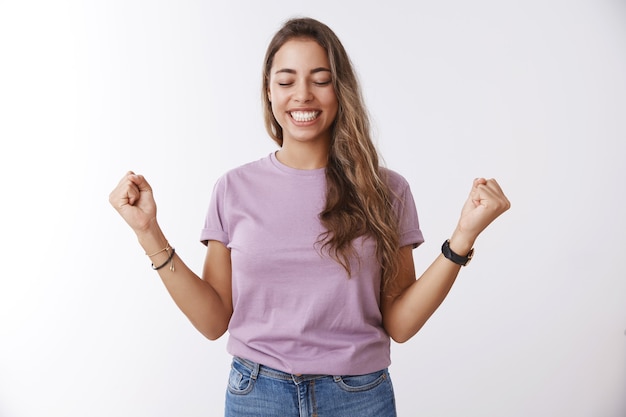 Oh, sí, finalmente la victoria. Feliz y atractiva estudiante encantadora aliviada obteniendo una beca universitaria levantando puños cerrados alegría de éxito, celebrando la victoria, logrando el logro de la meta, sonriendo