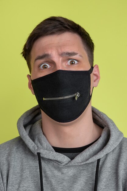 Ojos asustados. Retrato de hombre caucásico aislado en la pared amarilla del estudio. Modelo masculino extraño en mascarilla negra. Concepto de emociones humanas, expresión facial, ventas, publicidad. Apariencia inusual.