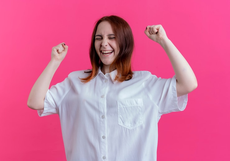 Foto gratuito con los ojos cerrados alegre joven pelirroja levantando puños aislados en rosa