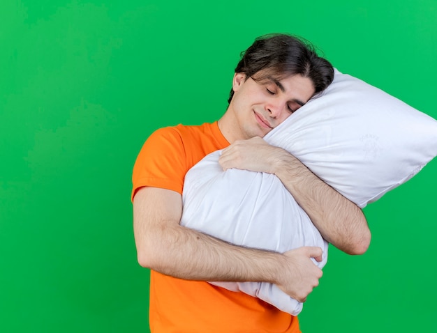 Con los ojos cerrados complacido joven enfermo abrazó la almohada aislada sobre fondo verde