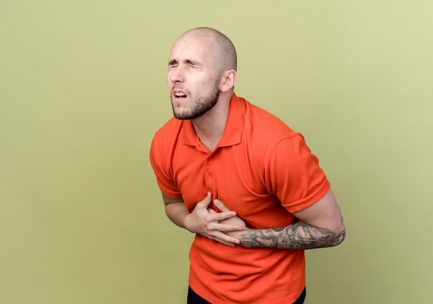 Foto gratuita con los ojos cerrados enfermo deportivo joven poniendo las manos en el pecho aislado en la pared verde oliva