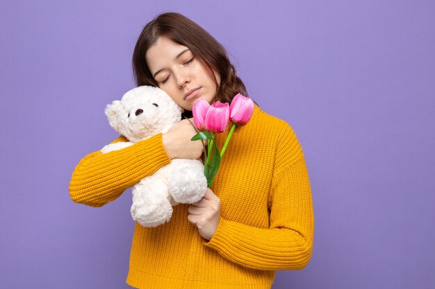 Con los ojos cerrados hermosa joven sosteniendo flores con osito de peluche