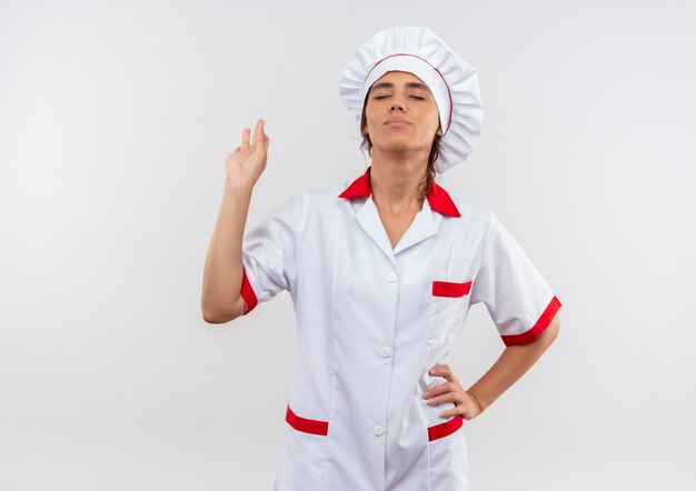 Con los ojos cerrados, joven cocinera complacida vistiendo uniforme de chef mostrando gesto okey con espacio de copia