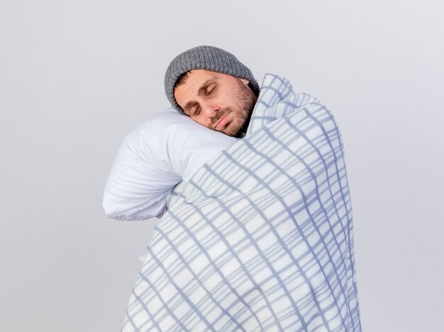 Con los ojos cerrados, el joven enfermo vestido con gorro de invierno y bufanda envuelto en una almohada plaid