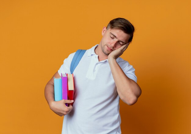 Con los ojos cerrados, joven y guapo estudiante masculino con bolsa trasera sosteniendo libros