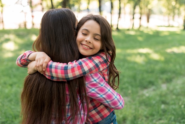 Ojos cerrados sonriendo linda niña abrazando a su madre en el parque