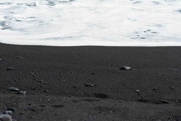 La ola oceánica con espuma blanca rueda sobre la playa de arena negra con guijarros.