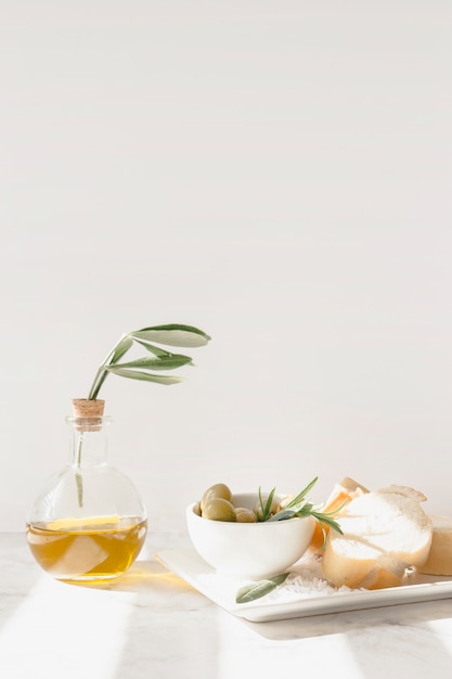 Oliva con una rodaja de pan y una botella de aceite contra la pared blanca