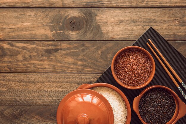 Una olla abierta y cuencos con diferentes tipos de granos de arroz en la mesa de madera