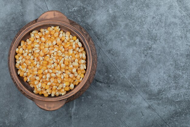 Olla antigua llena de palomitas de maíz crudas sobre un gris