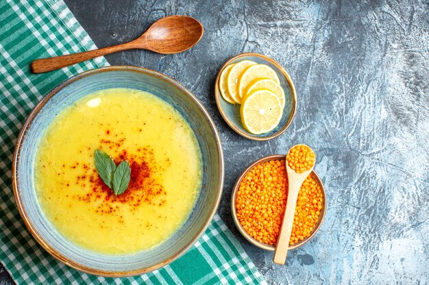 Una olla azul con una sabrosa sopa servida con menta y pimienta junto a una cuchara de madera de limón picado y un guisante amarillo sobre fondo azul.