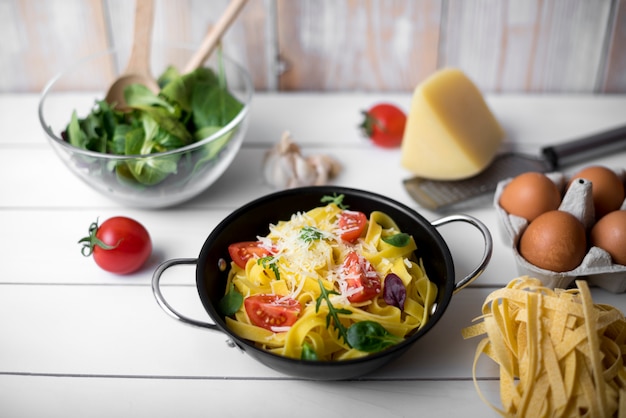 Olla de cocción rellena de pasta e ingredientes de tallarines saludables en una mesa de madera blanca