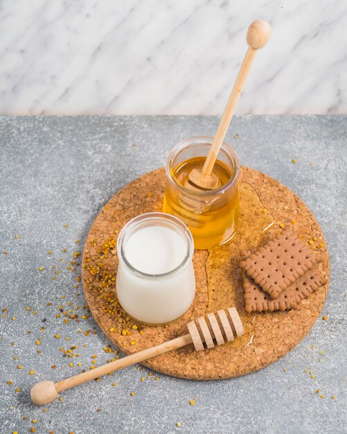 Olla de leche y miel con galletas horneadas y cucharón de miel en montaña de corcho