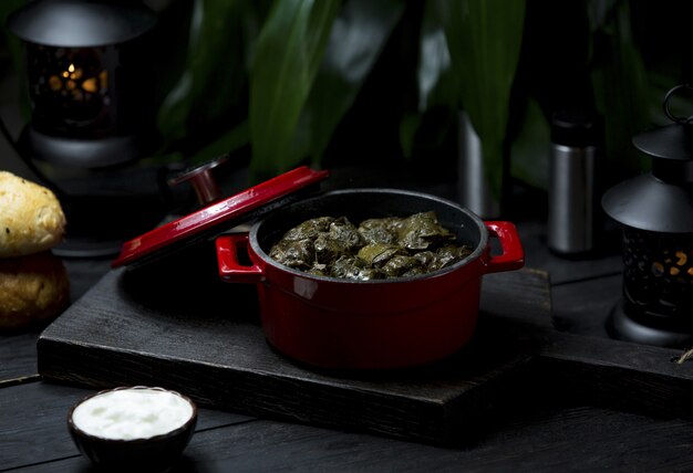 Una olla roja de comida local yarpaq dolmasi, sarma en un tablero oscuro