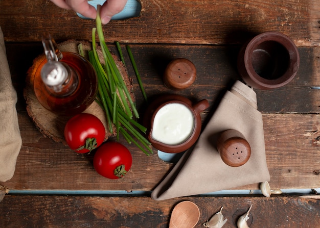 Una olla de yogurt, tomates, hierbas y una botella de oliva en la mesa de madera Vista superior