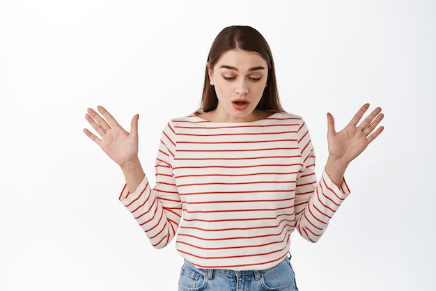 Oops, se le cayó algo. La chica jadeante levanta las manos hacia los lados y mira hacia abajo sorprendida, ve algo debajo de pie emboscado contra el fondo blanco.