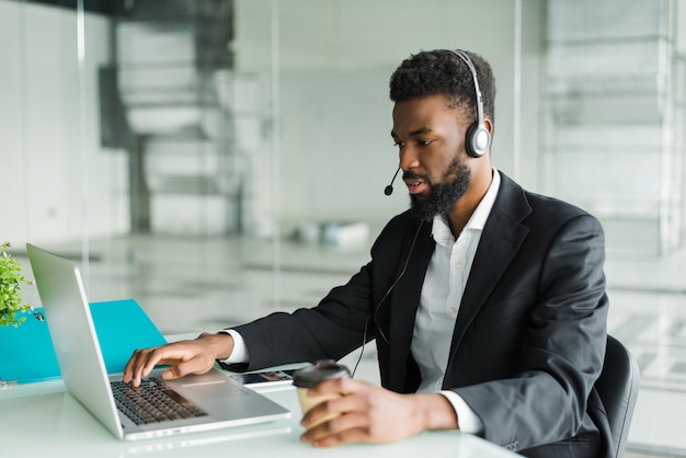 Operador de atención al cliente hombre afroamericano con auriculares manos libres trabajando en la oficina.