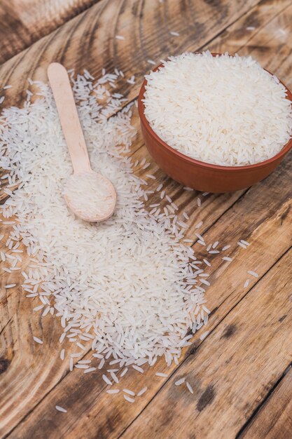 Opinión de alto ángulo del arroz crudo fresco en cuenco con la pequeña cuchara sobre fondo de madera texturizado
