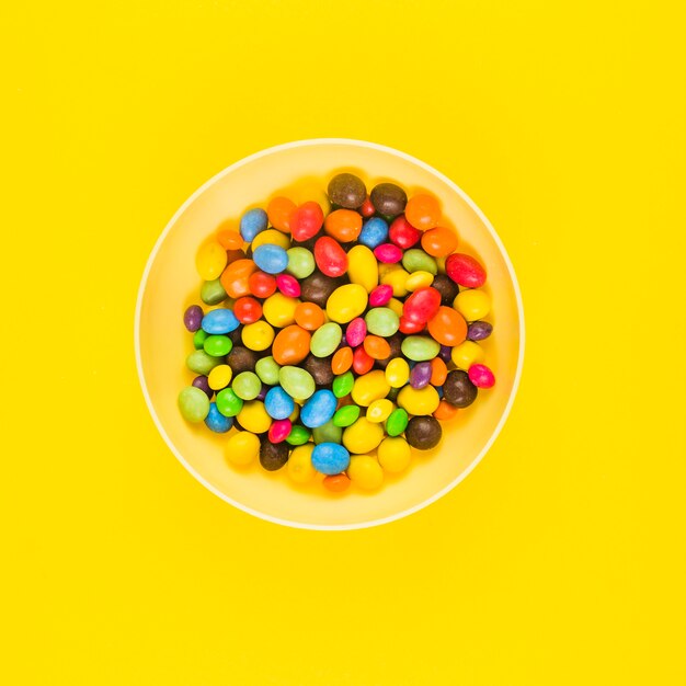Opinión de alto ángulo de caramelos dulces coloridos en la placa sobre superficie amarilla