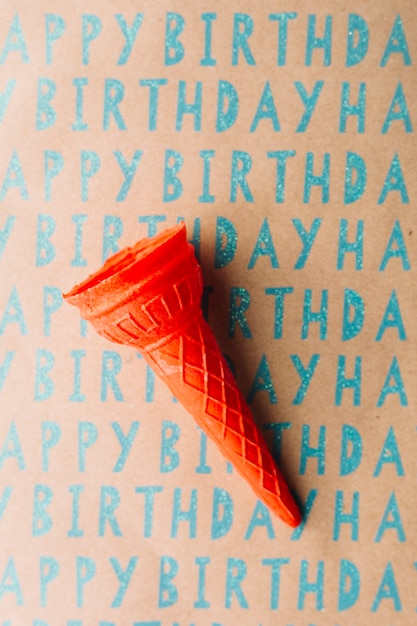 Opinión de alto ángulo del cono de helado vacío en el papel del regalo del feliz cumpleaños