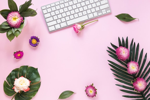 Opinión de alto ángulo de flores y del teclado coloridos en fondo rosado