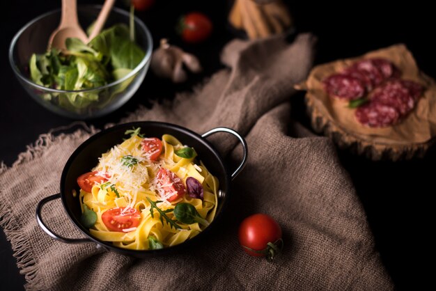 Opinión de alto ángulo de las pastas sanas en cocinar el pote en la materia textil del yute con el tomate y la ensalada de cereza