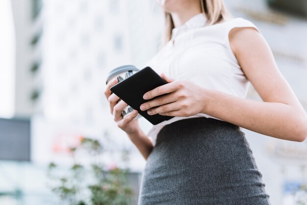 Opinión de ángulo bajo de la empresaria que sostiene smartphone y la taza de café disponible en al aire libre