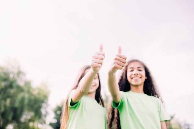 Opinión de ángulo bajo de las muchachas lindas que muestran el pulgar encima del gesto contra el cielo