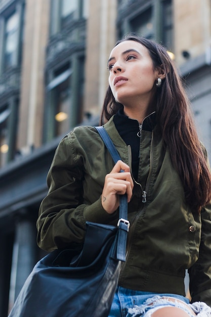 Foto gratuita opinión de ángulo bajo la mujer joven que sostiene el bolso azul que camina en la calle