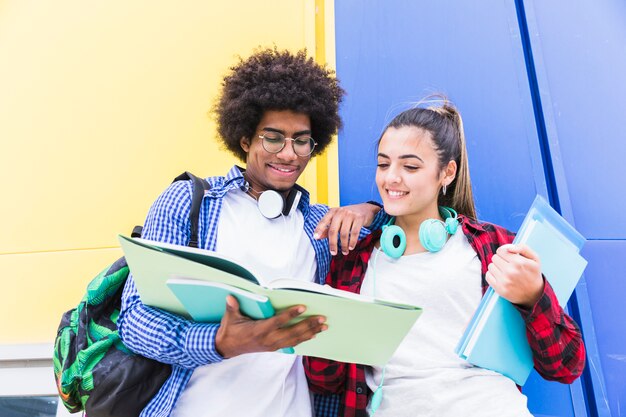 Opinión de ángulo bajo de los pares adolescentes que leen el libro que está parado contra la pared coloreada