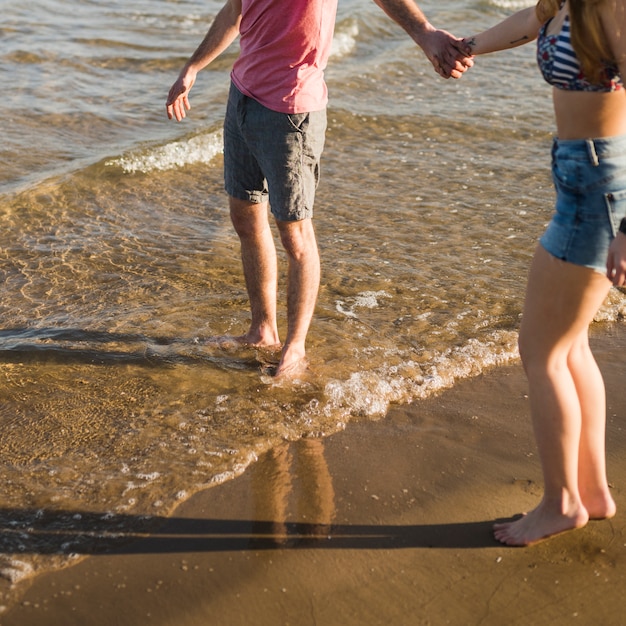 Foto gratuita opinión de ángulo bajo de los pares jovenes que se sostienen la mano de cada uno que se coloca cerca de la costa de mar