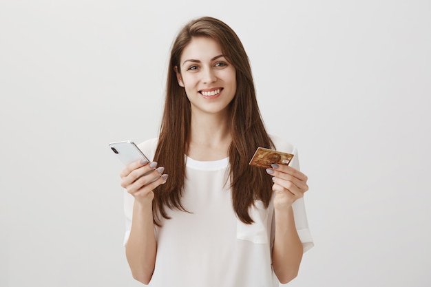 Orden de mujer sonriente feliz en línea a través de la aplicación de teléfono inteligente, con tarjeta de crédito y teléfono móvil