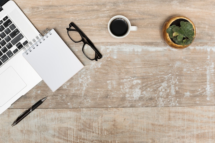 Foto gratuito ordenador portátil; bloc de notas espiral los anteojos; té negro y planta en mesa de madera
