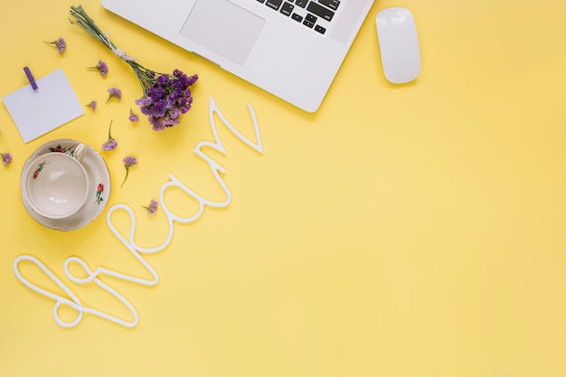 Foto gratuita ordenador portátil; flores púrpuras con palabra de sueño y taza vacía sobre fondo amarillo