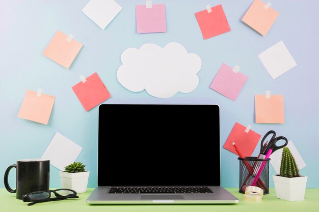 Ordenador portátil frente a la pared con papel de nubes y notas adhesivas