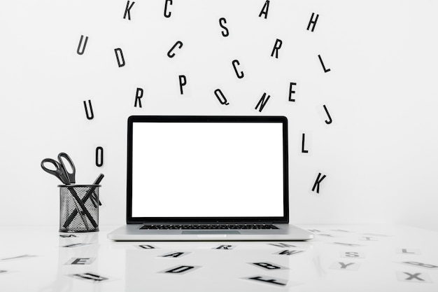 Ordenador portátil con pantalla blanca en blanco cerca de portalápices y alfabetos en superficie blanca