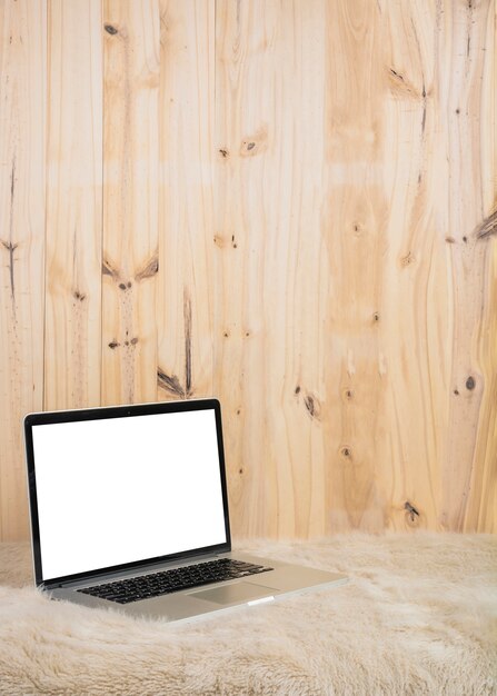 Ordenador portátil con pantalla en blanco en blanco sobre piel suave frente a pared de madera