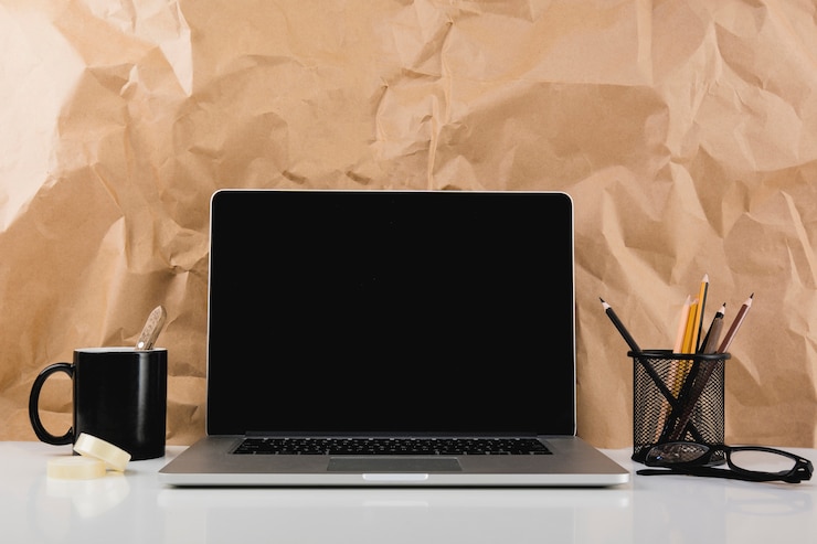Foto gratuito ordenador portátil con pantalla negra en blanco delante de la textura de papel marrón