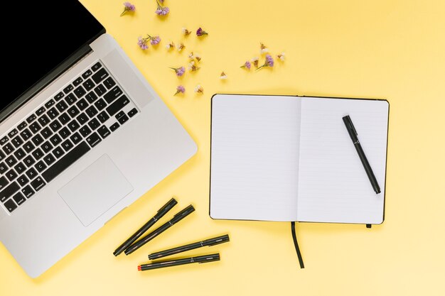 Ordenador portátil con rotuladores; cuaderno en blanco con flores de lavanda sobre fondo amarillo