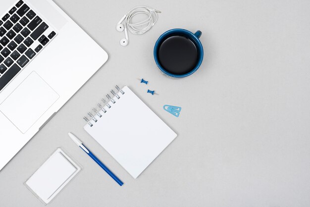 Ordenador portátil; Taza de café con papelería de oficina y auricular sobre el escritorio de negocios gris